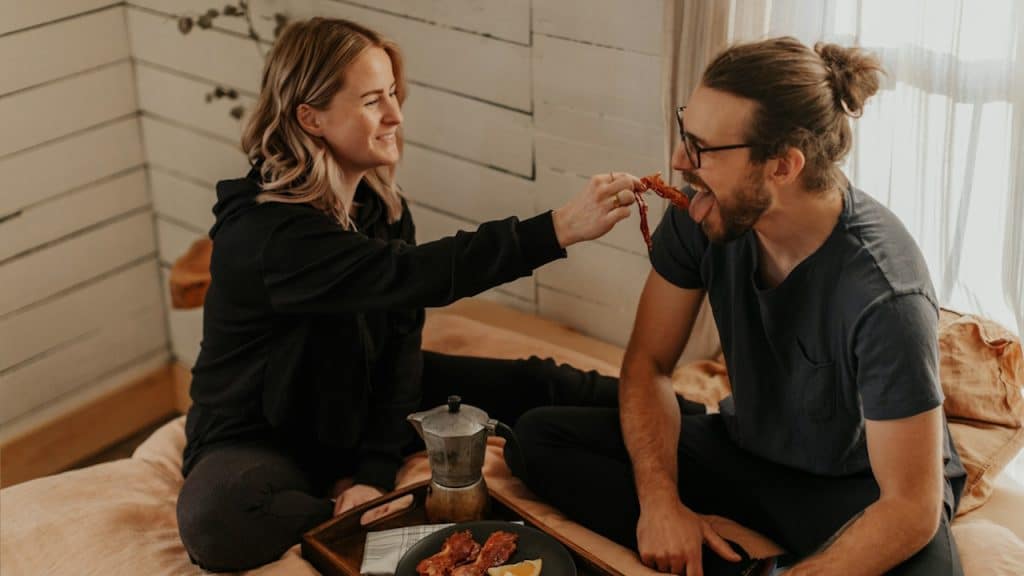 A woman feeding chicken wings to her man.