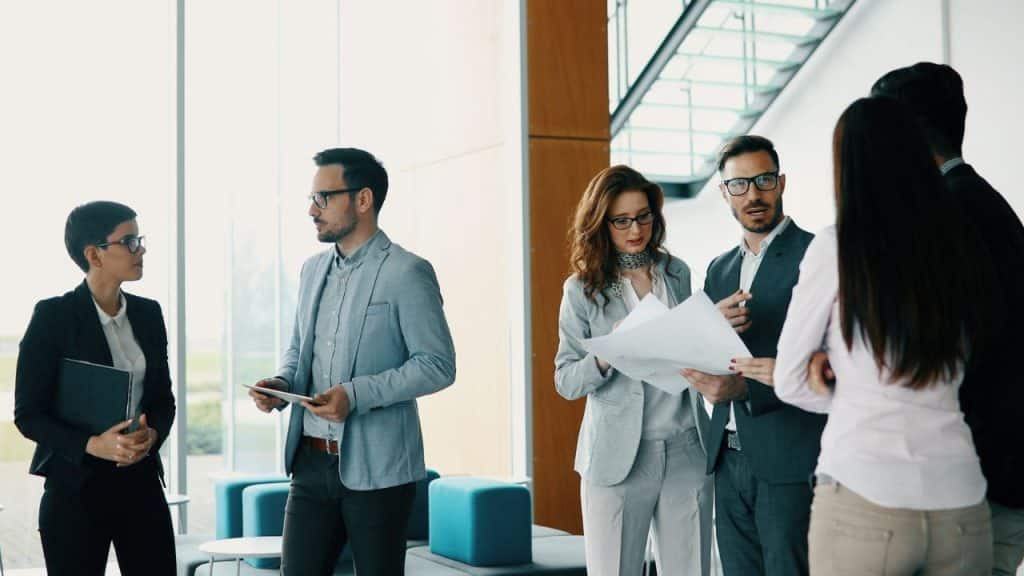 Three men and three women in business attire stand in a modern office lobby.