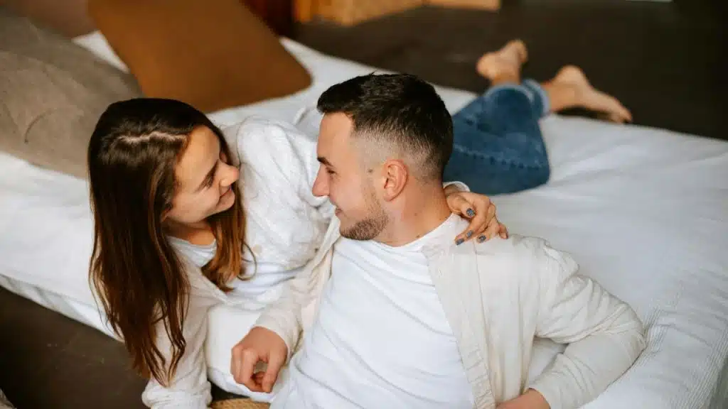 A smiling man and woman are lying on a bed, looking at each other.