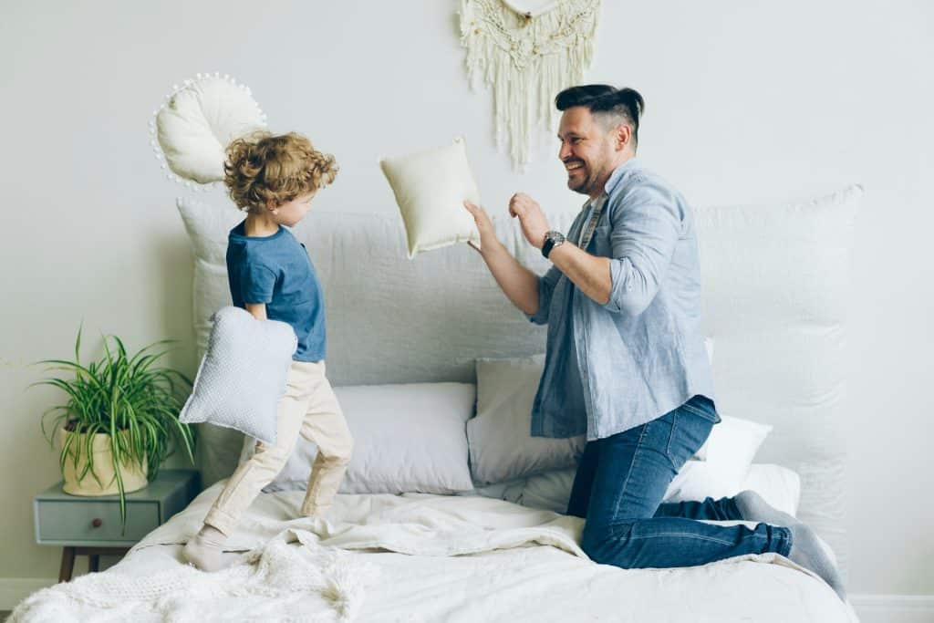The Dad is playing with pillows with his son.