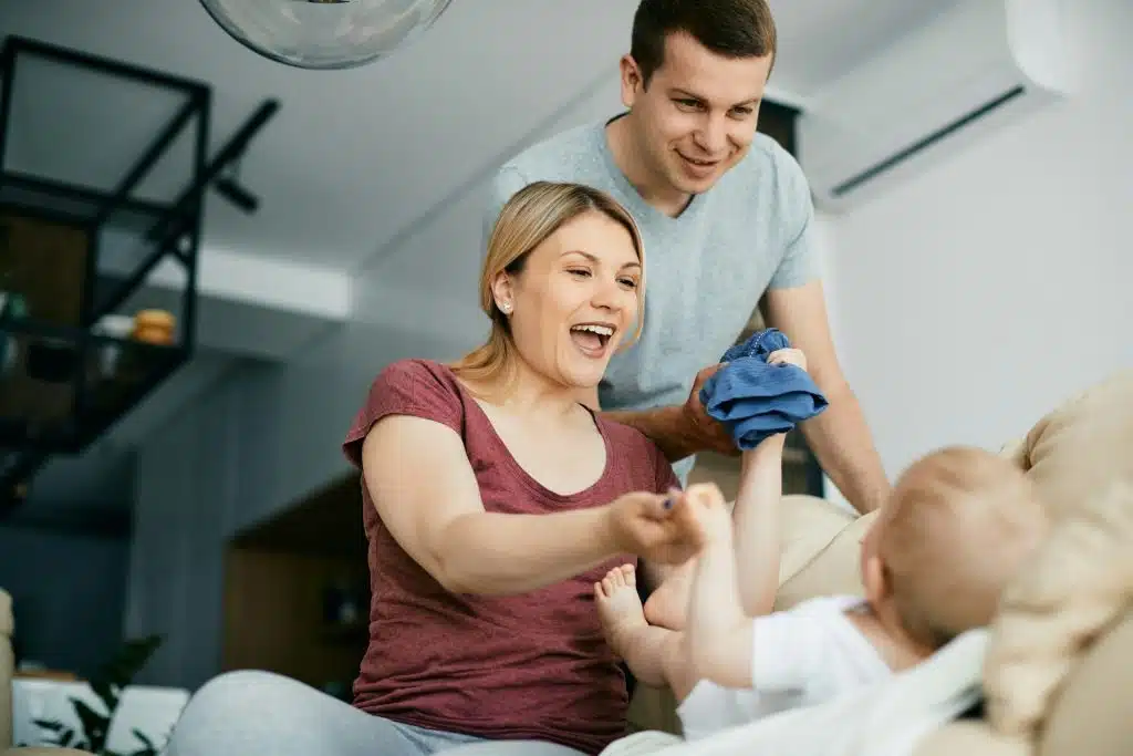 The couple is dressing up the baby in the living room.