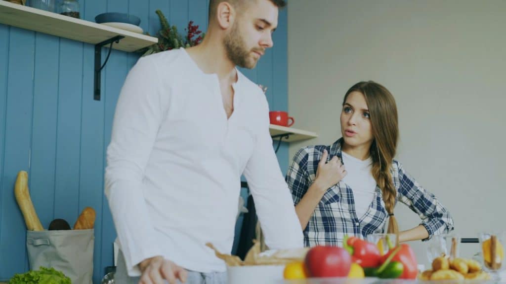 A man in a white shirt and a woman in a plaid shirt are arguing in a kitchen.
