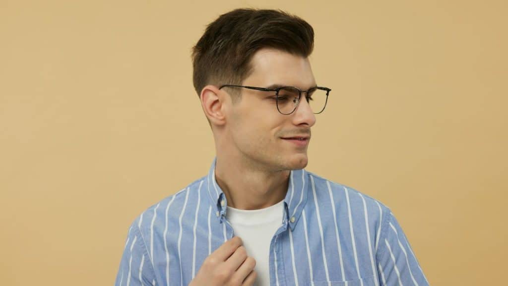 A man wearing round glasses and a blue striped shirt looks away from the camera.