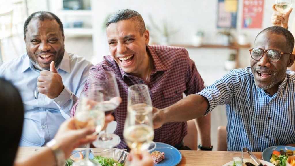 Three laughing men seated at a table, raising glasses for a toast.