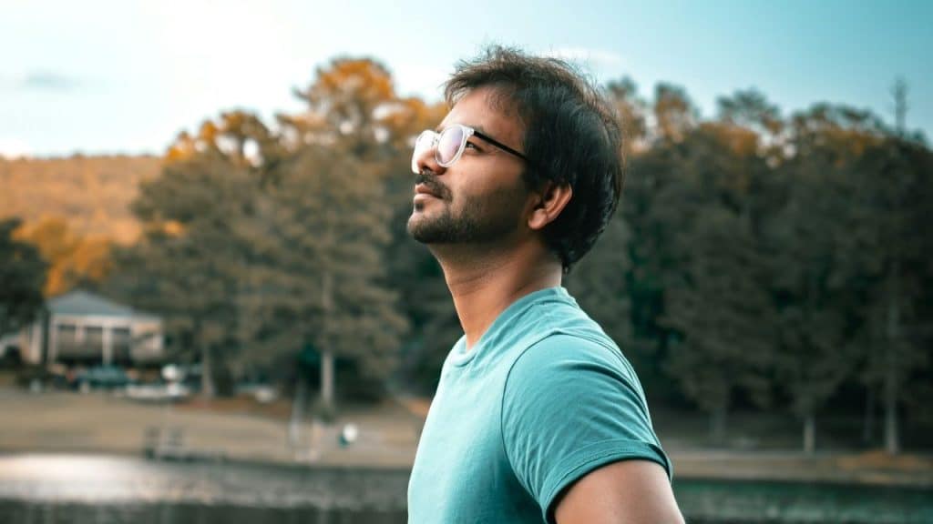 Man in teal shirt and glasses looking up against a blurry outdoor background.