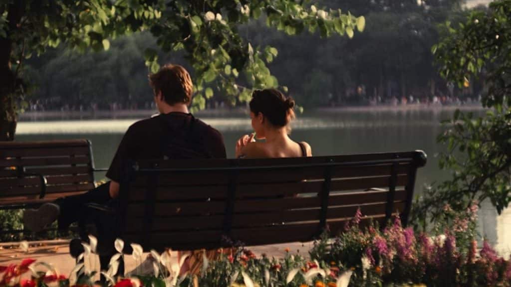 Couple sitting on a park bench, man looking hopeful while woman looks distant