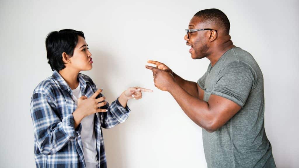A man and woman face each other, pointing fingers and arguing against a white background.
