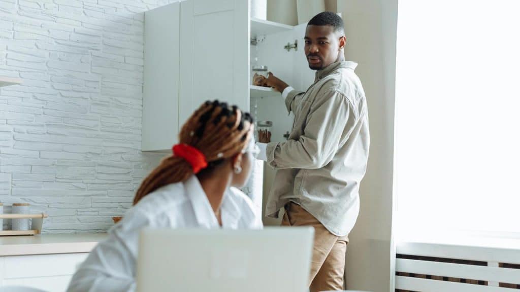 A man looking at a woman while reaching into a kitchen cabinet.