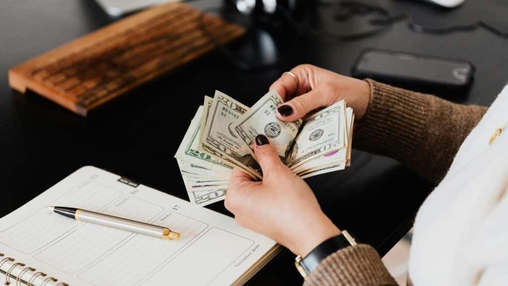A person counting dollar bills at a desk with a notebook and pen.