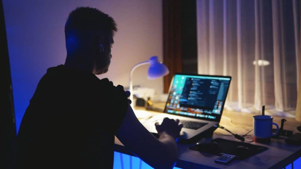 Person sitting at a desk working on a laptop in a dimly lit room at night.