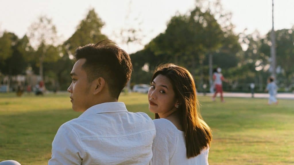 A man and woman in a park with the woman looking backwards at the camera.