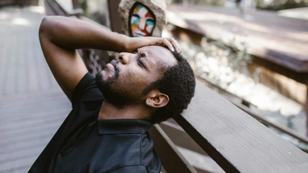 A man sitting outdoors with his hand on his head, appearing stressed or tired.