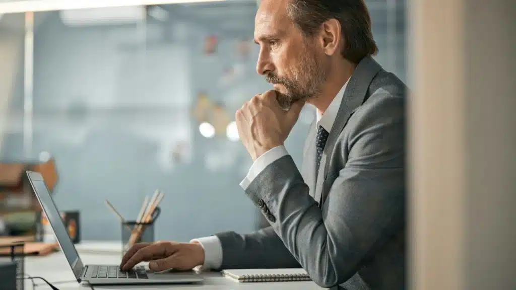 Middle-aged businessman in a suit working intently on a laptop at his desk.