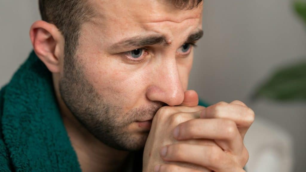 Close-up of a man with blue eyes, hands clasped near his mouth.