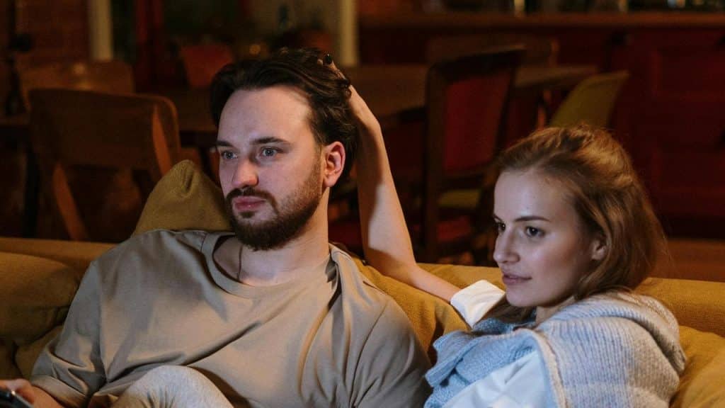 A couple sitting on a couch watching something together.