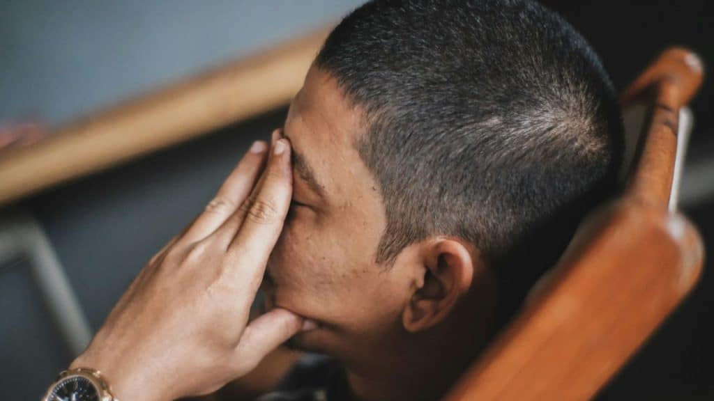 Close-up of person with short hair covering their eyes with one hand.
