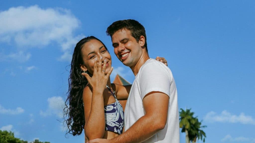 A smiling couple posing outdoors under a bright blue sky.