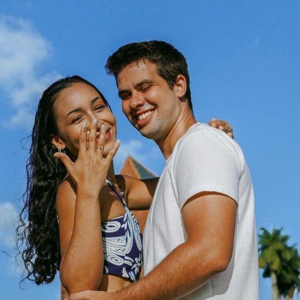 A smiling couple posing outdoors under a bright blue sky.