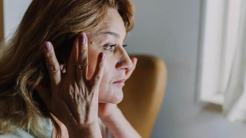 A woman touching her face while looking out a window.