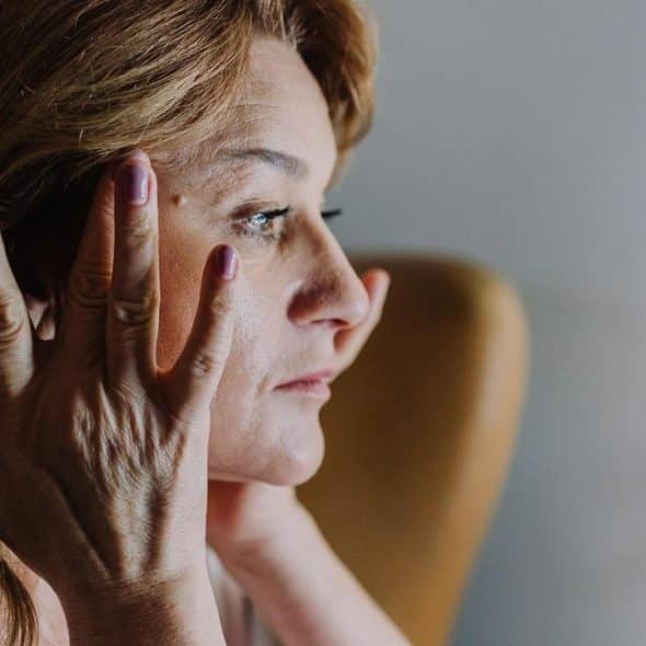 A woman touching her face while looking out a window.
