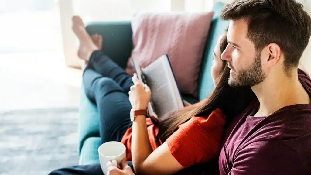 A bearded man and a woman cuddling on a teal couch.