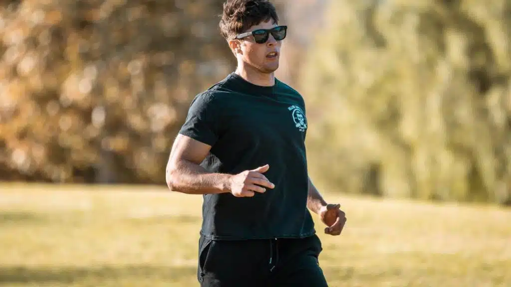 A man jogging outdoors wearing a black shirt and sunglasses.