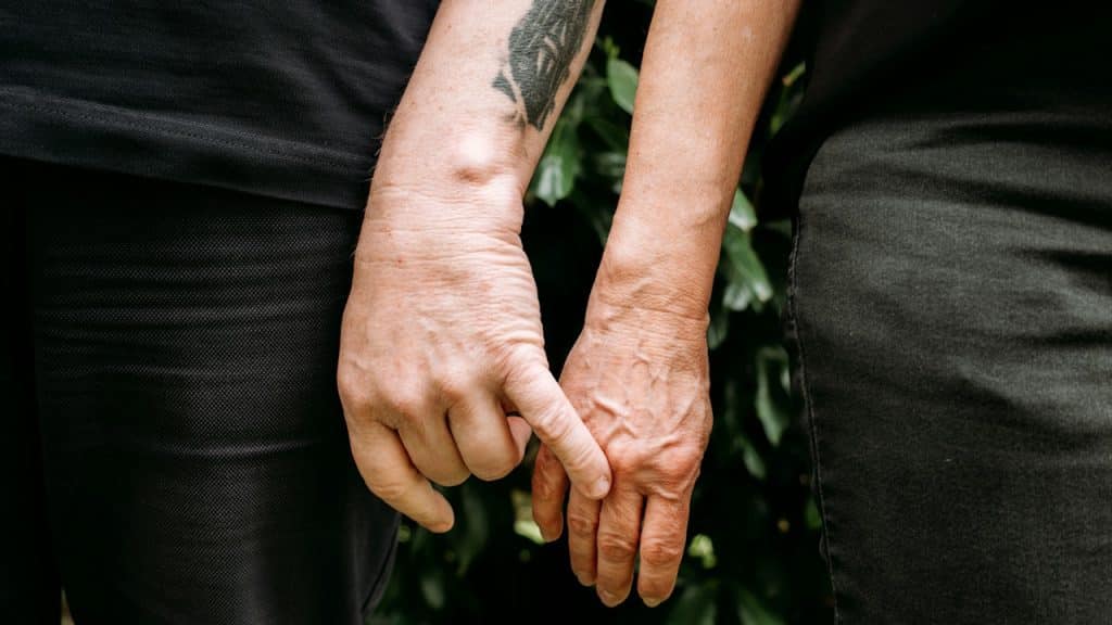 A close-up of two people holding hands by linking their index fingers, with one arm having a tattoo.
