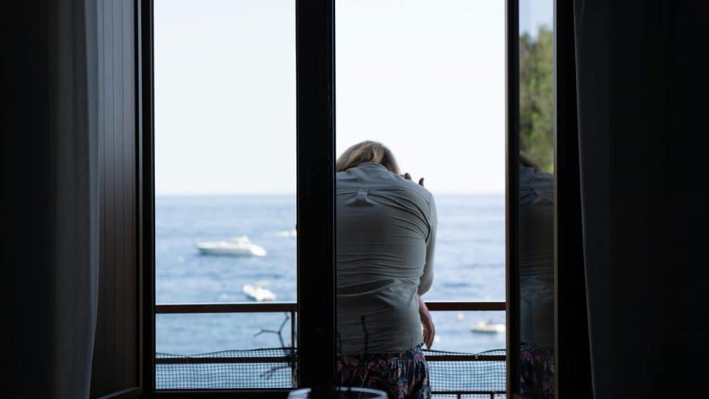 A woman leaning on a balcony railing looking out at the ocean.