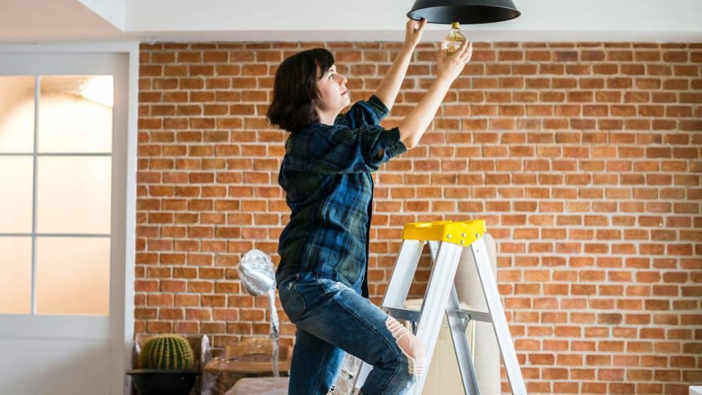 A woman standing on a ladder changing a light bulb.