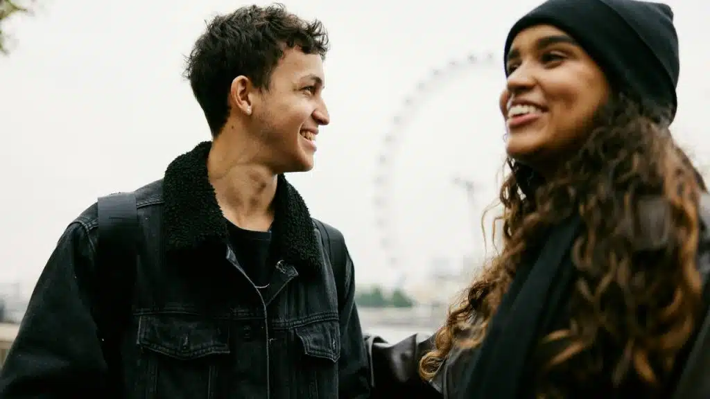 A smiling couple talking outdoors, with a Ferris wheel in the background.