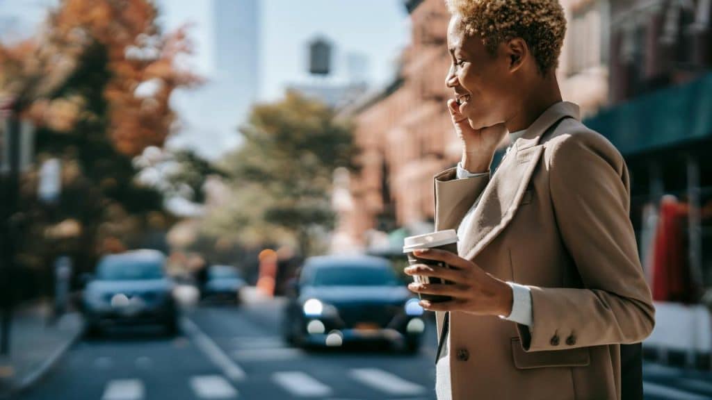 A person walking in the city while talking on the phone and holding a coffee cup.