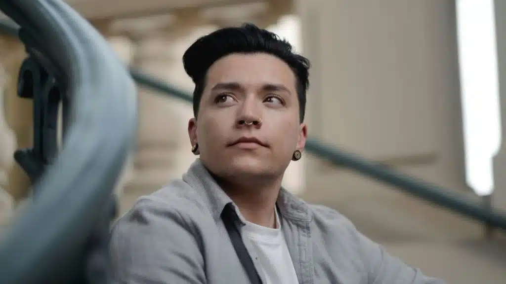 A young person with black hair and a nose ring is looking up thoughtfully.