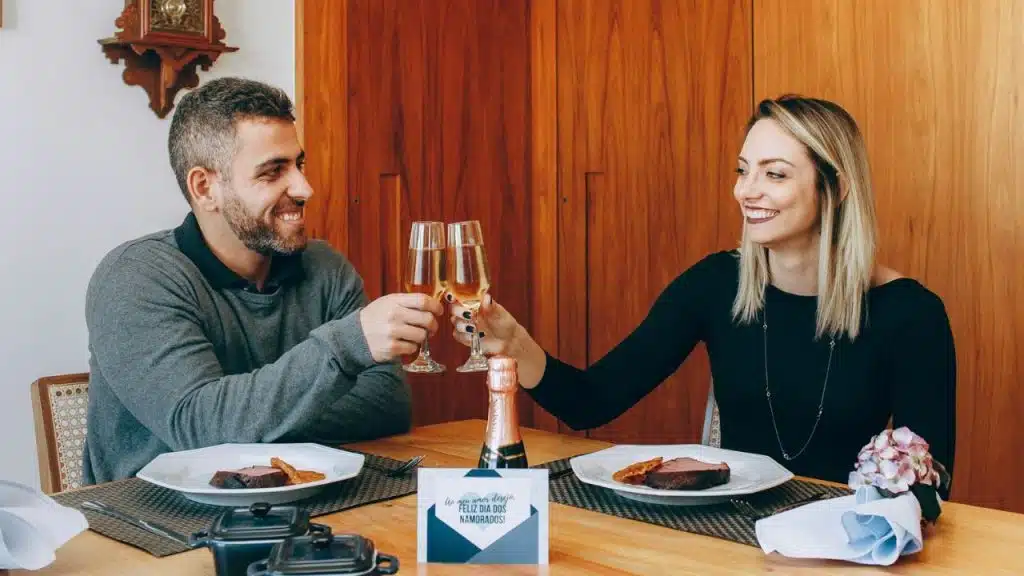 Smiling man and woman toasting with champagne flutes at a dinner table.