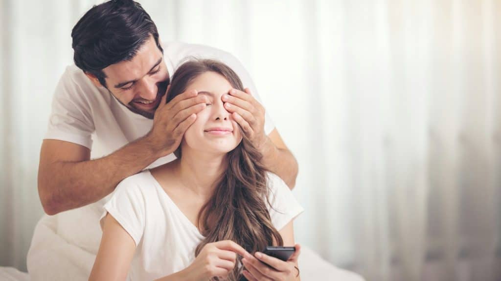 A young man covering the eyes of his wife.