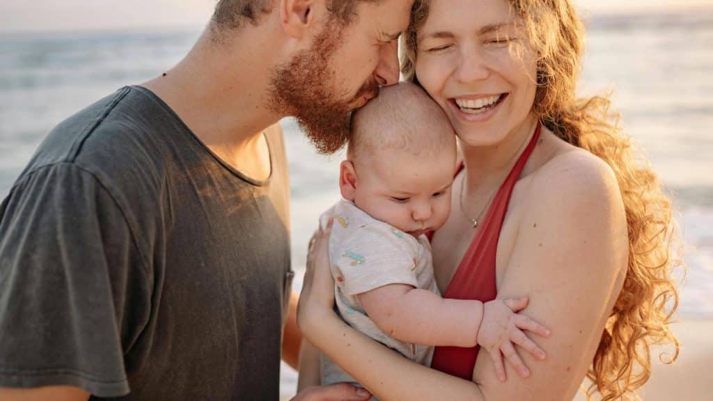 A smiling couple holding their baby on the beach.
