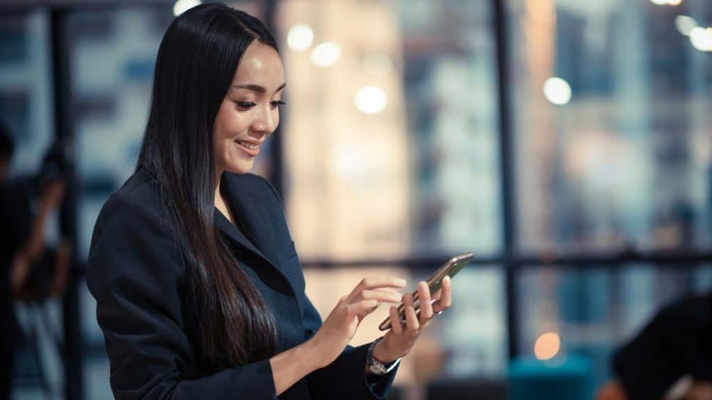 A woman smiling while using her smartphone indoors.