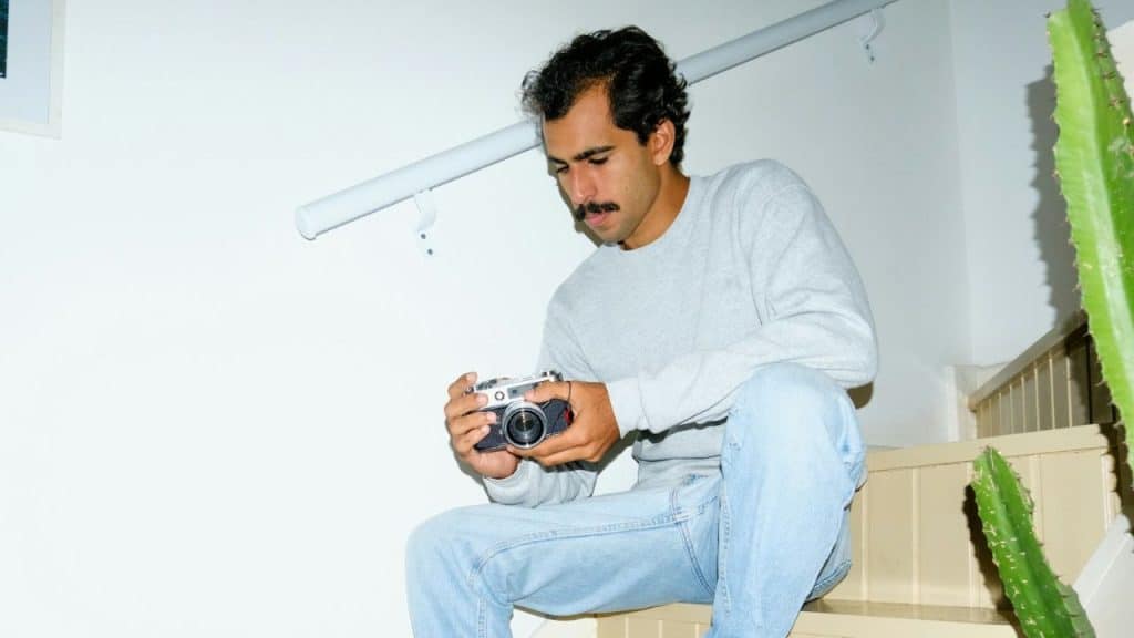 A man with a mustache sits on a staircase, examining an old-fashioned film camera.