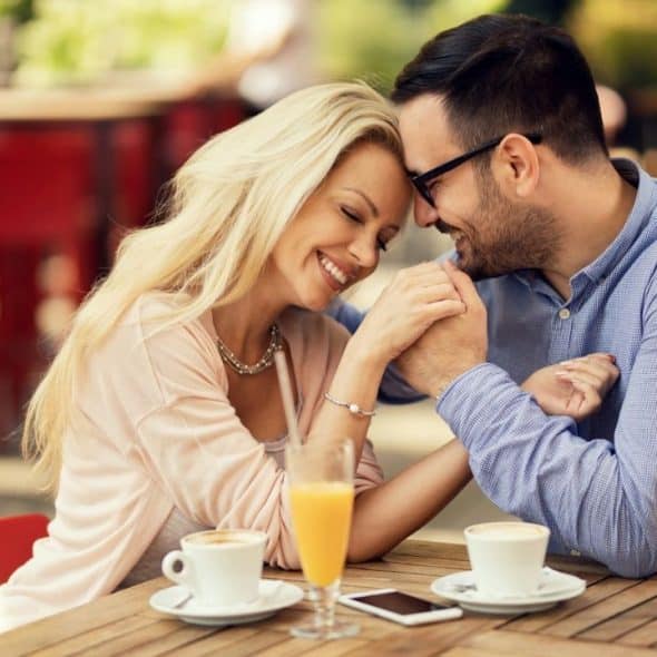 A man and woman smiling and holding hands across a cafe table outdoors.