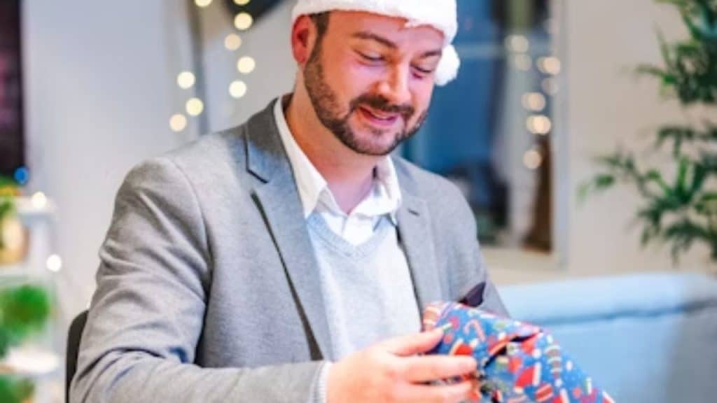 Man wrapping holiday gifts at home with thoughtful expression
