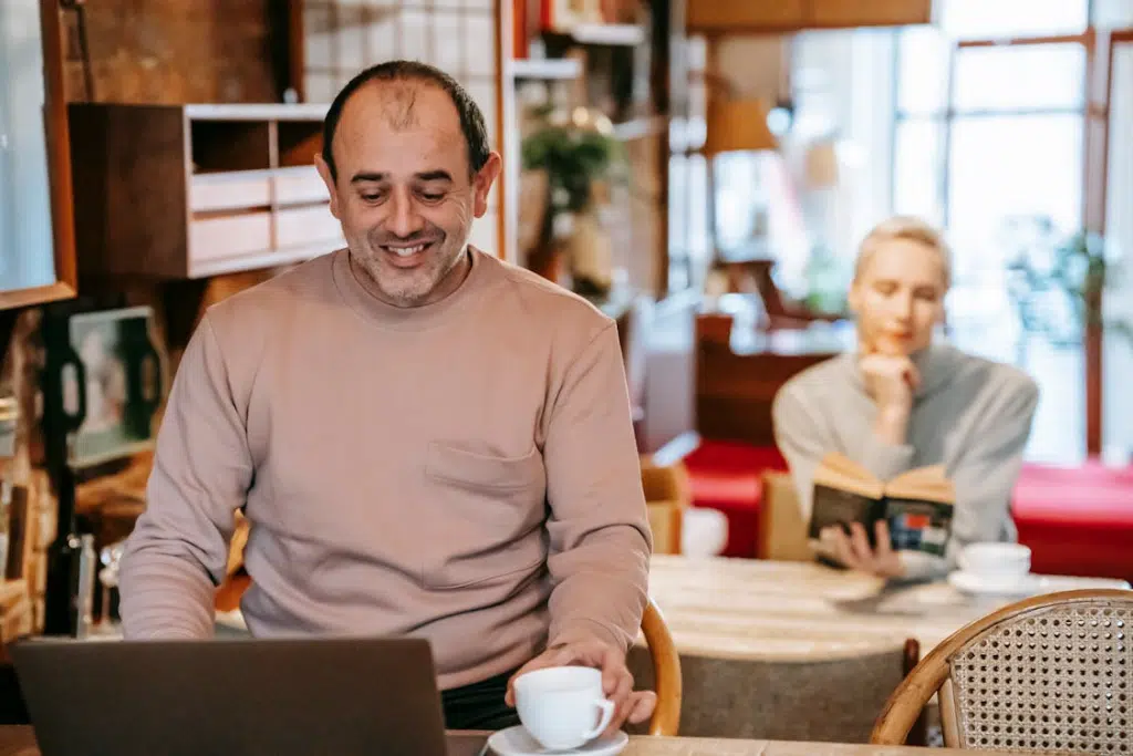 Smiling man working online on netbook near wife reading novel