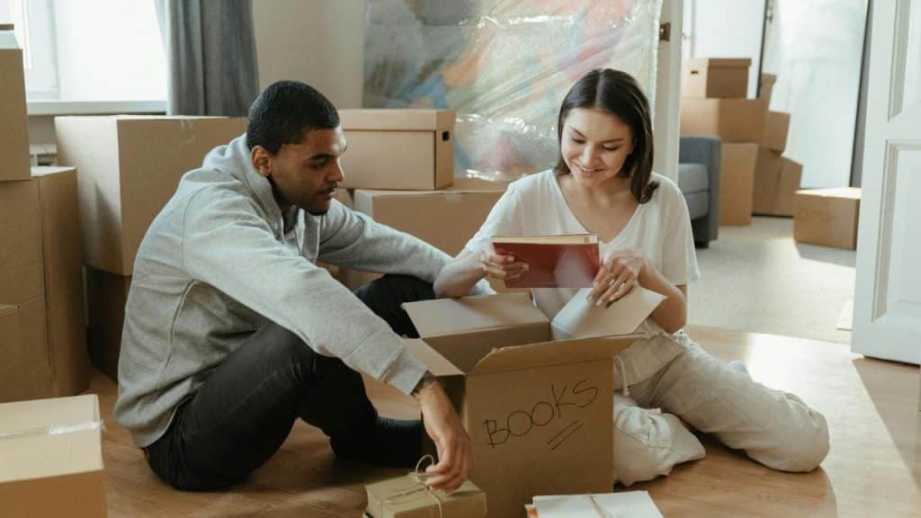 A couple sitting on the floor unpacking books from moving boxes.