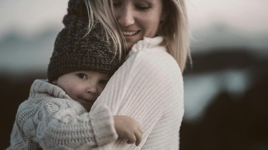 A mother hugging her child outdoors on a cool day.