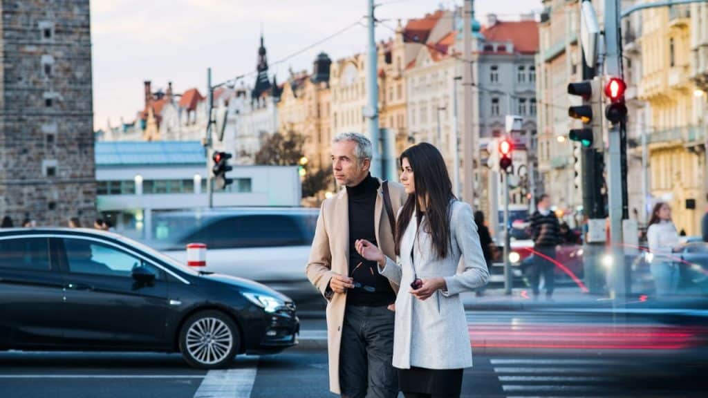 Man and woman walking on a city crosswalk with blurred car lights and buildings.