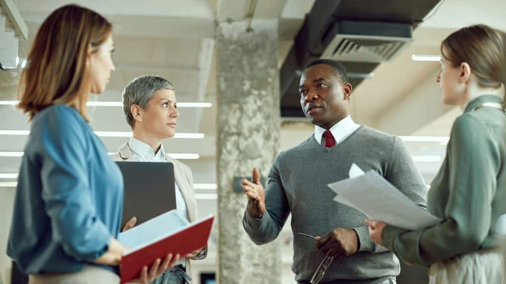 Four business professionals stand in an office, engaged in a focused conversation.