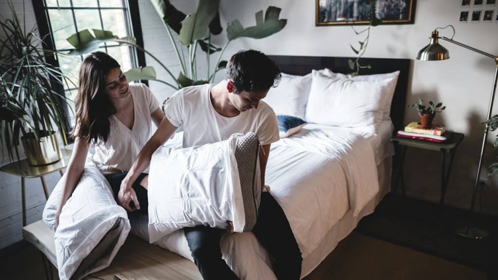 A couple sitting on a bed holding pillows.