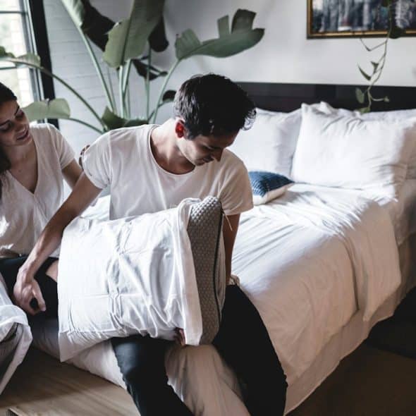 A couple sitting on a bed holding pillows.