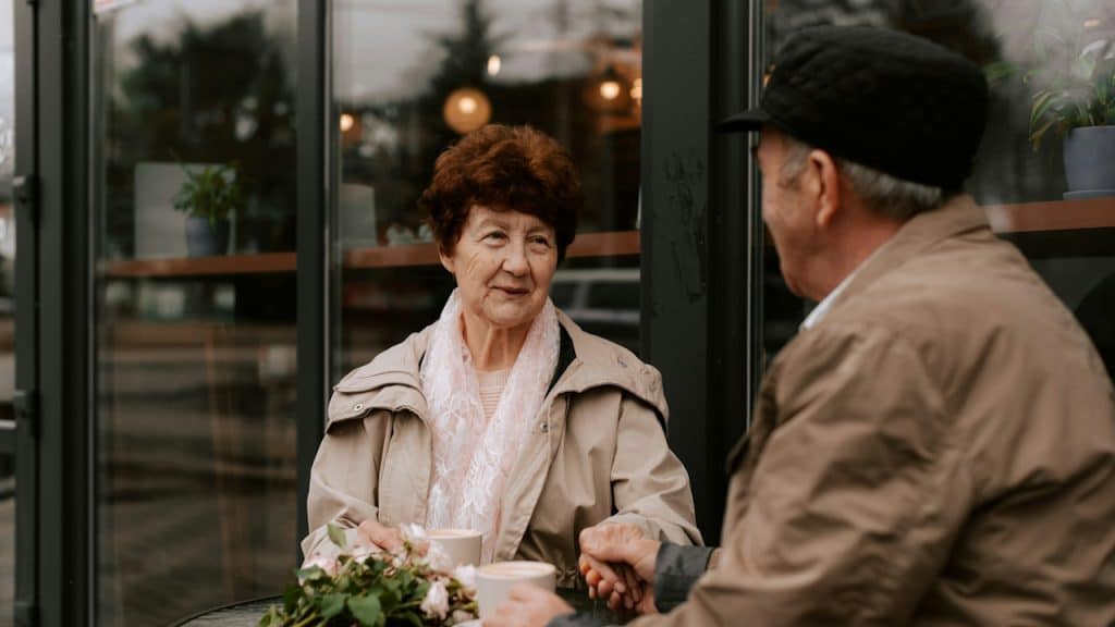 A man and woman having coffee while sitting at a table outdoors.