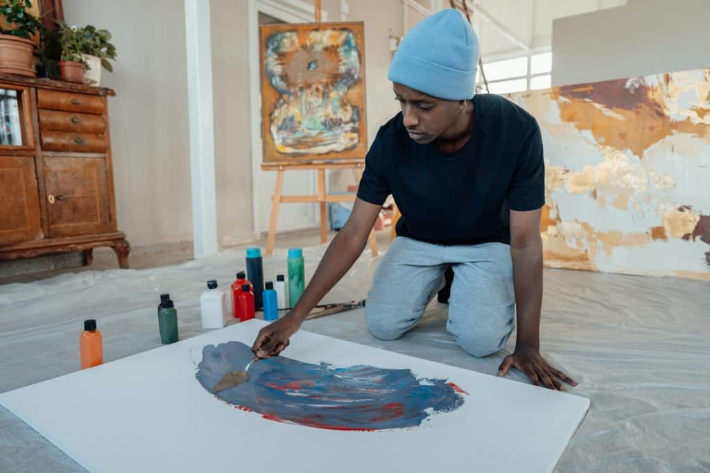 The man in a blue hat is painting on a canvas.