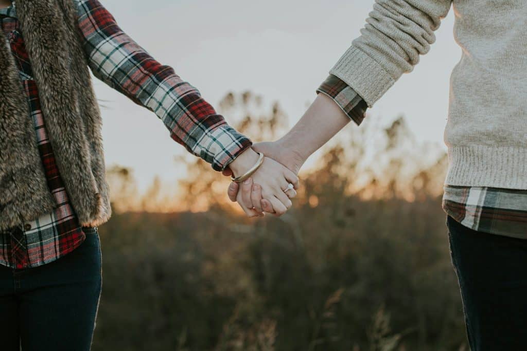 The couple is holding hands while standing.