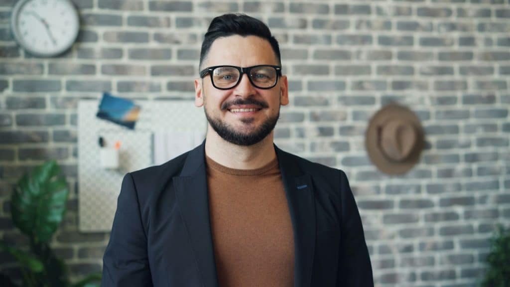 A man wearing glasses standing in front of a brick wall.